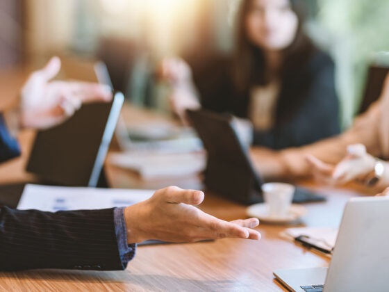 Image of a board room table with smartly dressed nondescript people sitting round it.